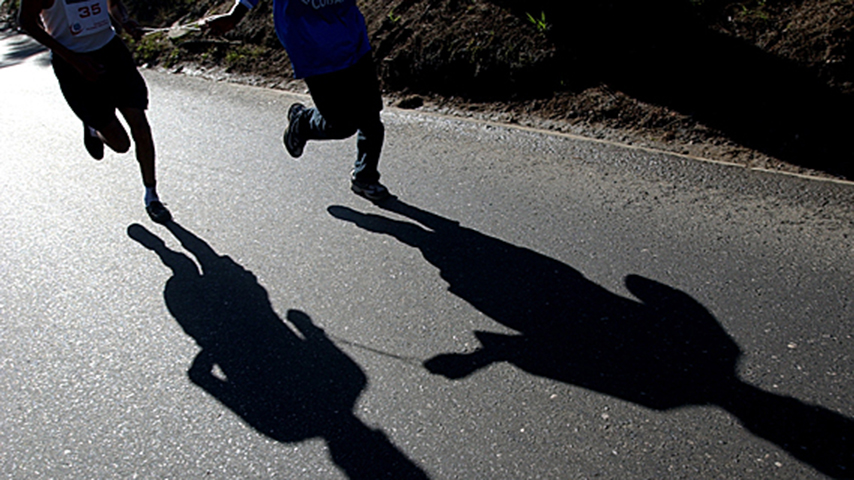 Two people running and their shadows are shown on the ground.